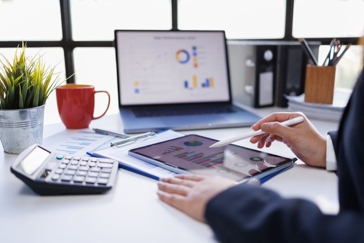 Person using a tablet to review accounting charts and financial data beside a calculator and laptop