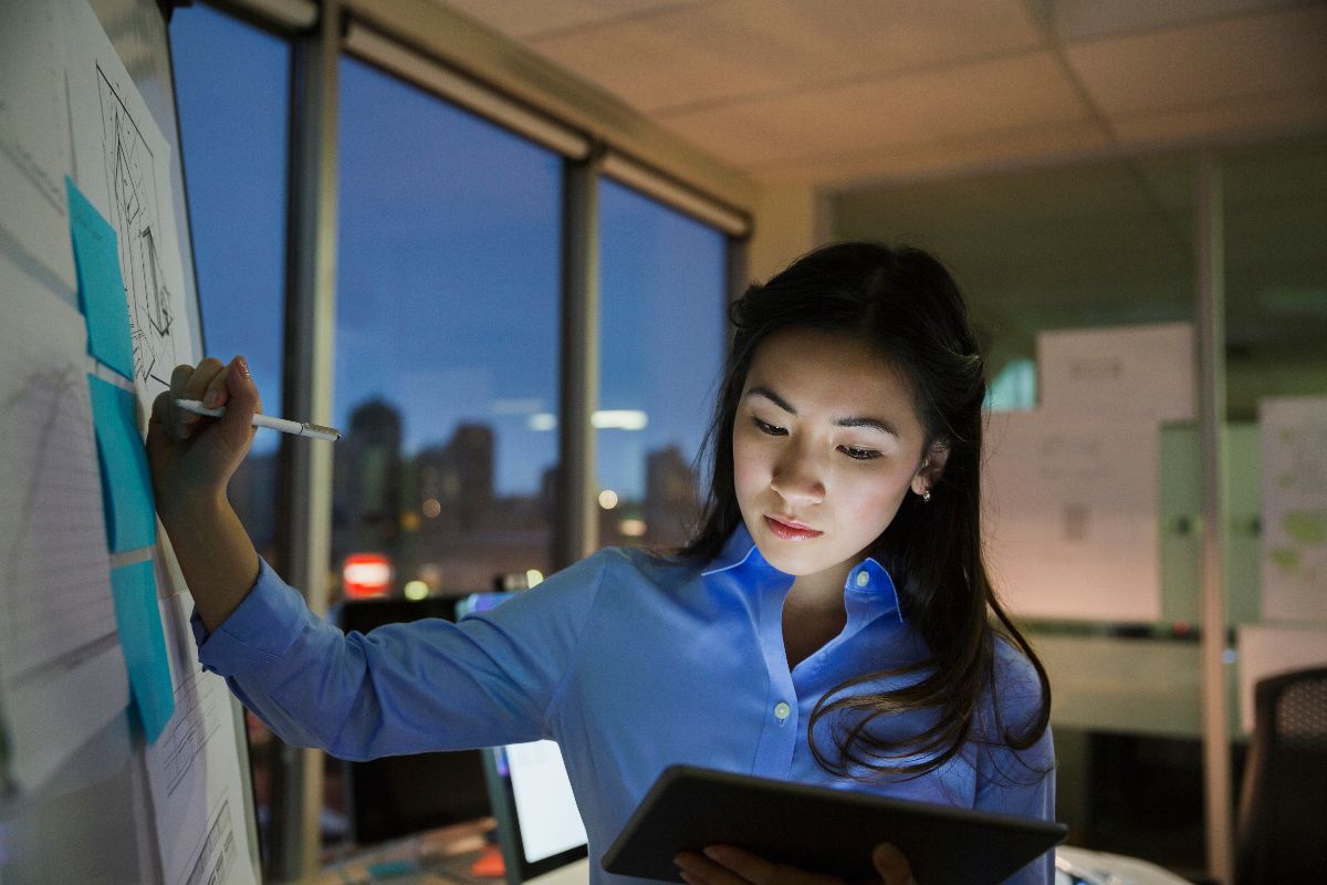 Business professional using a tablet while reviewing planning documents on a board, representing multi-entity accounting coordination.