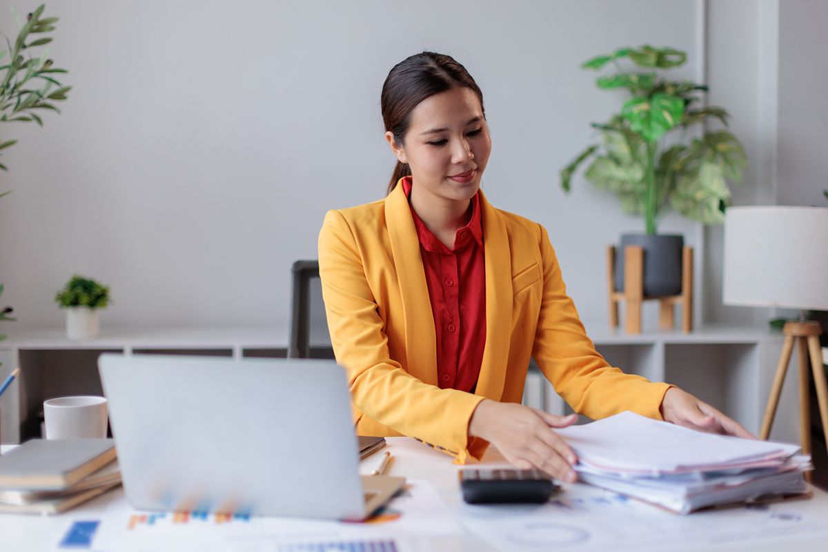 Business professional organizing financial documents beside a laptop in a modern office