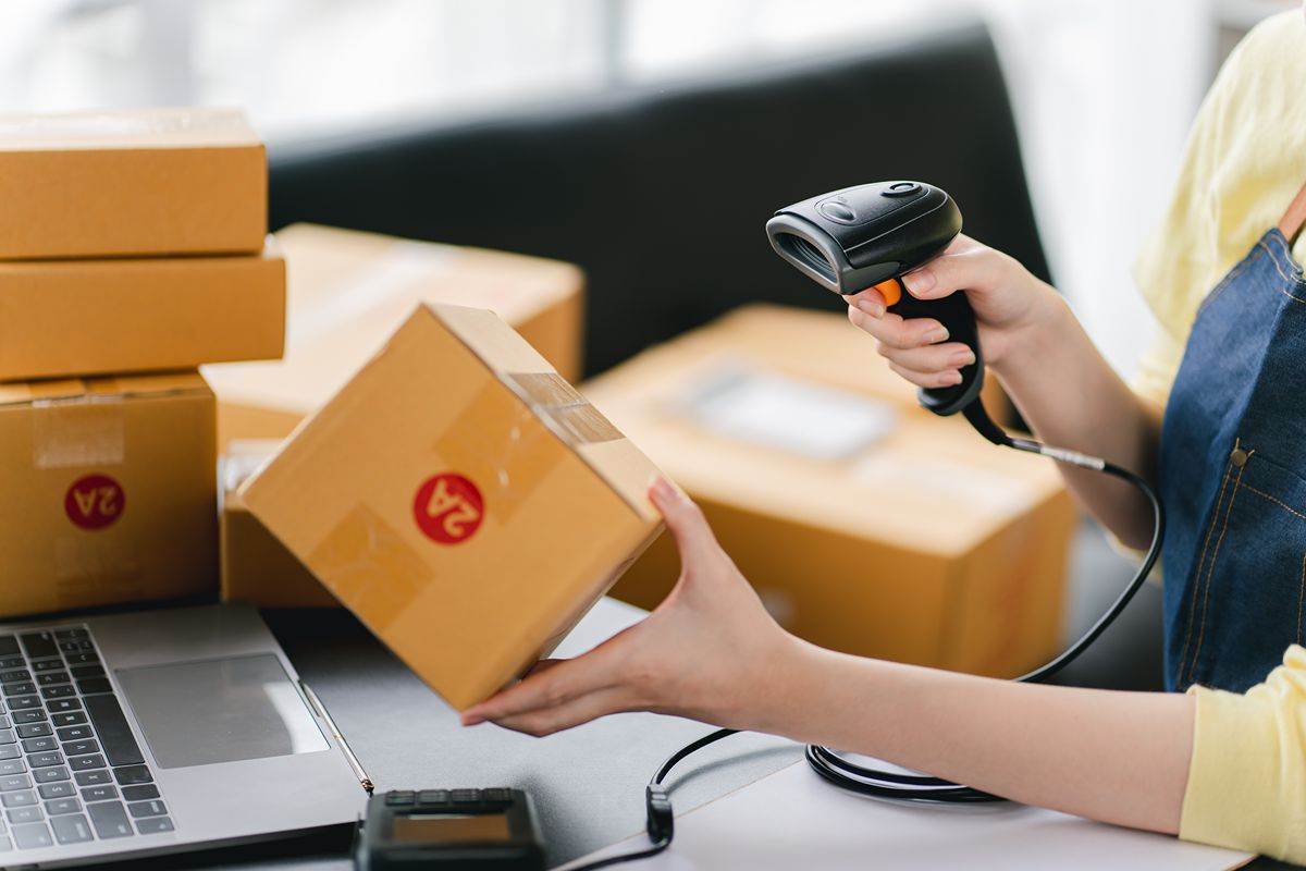 Worker scanning a package barcode beside a laptop in a warehouse