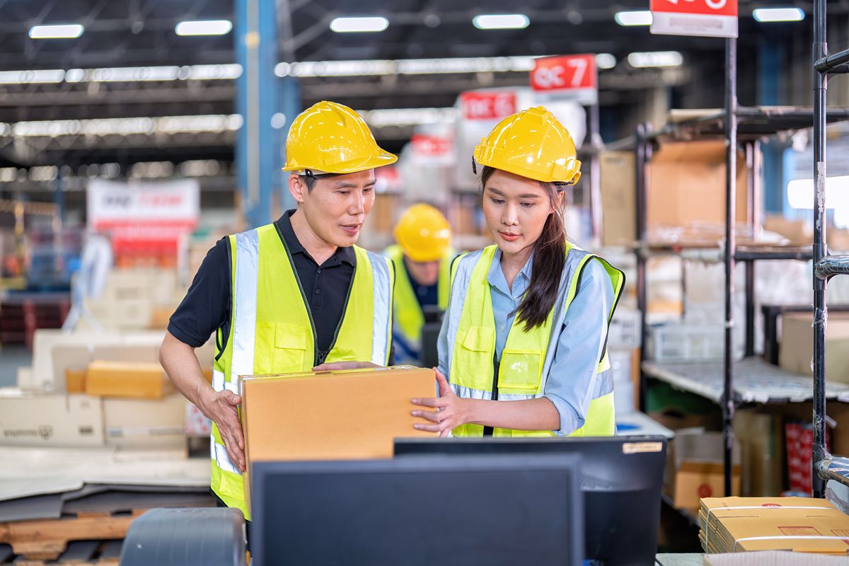 Two warehouse staff checking a package near storage racks and a computer