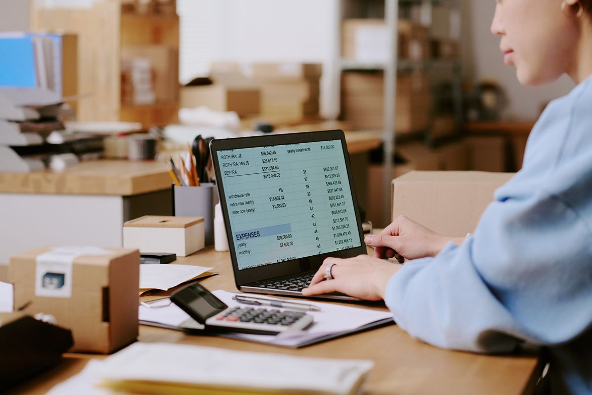 Employee reviewing inventory data on a laptop while managing stock across multiple storage locations