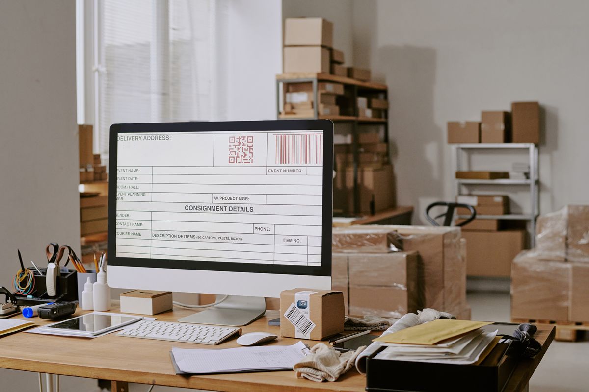 Warehouse workstation with inventory records on a desktop computer surrounded by packages and shipping materials