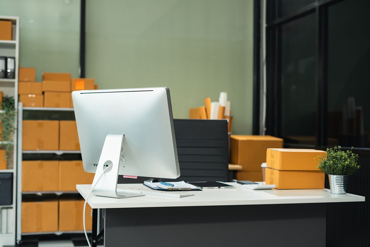 Warehouse office with desktop computer and packaged inventory representing centralized inventory management and connected operations