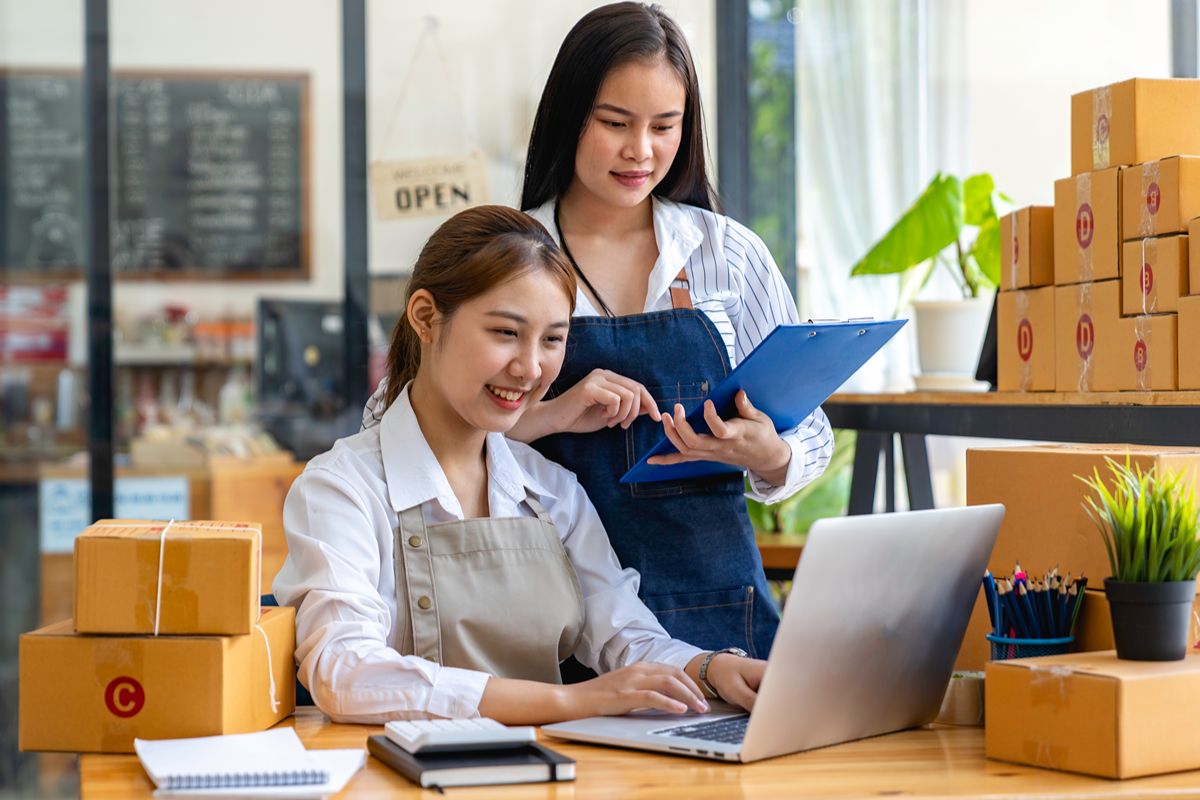 Two employees managing inventory and business records with a laptop and packaged goods in an integrated work environment