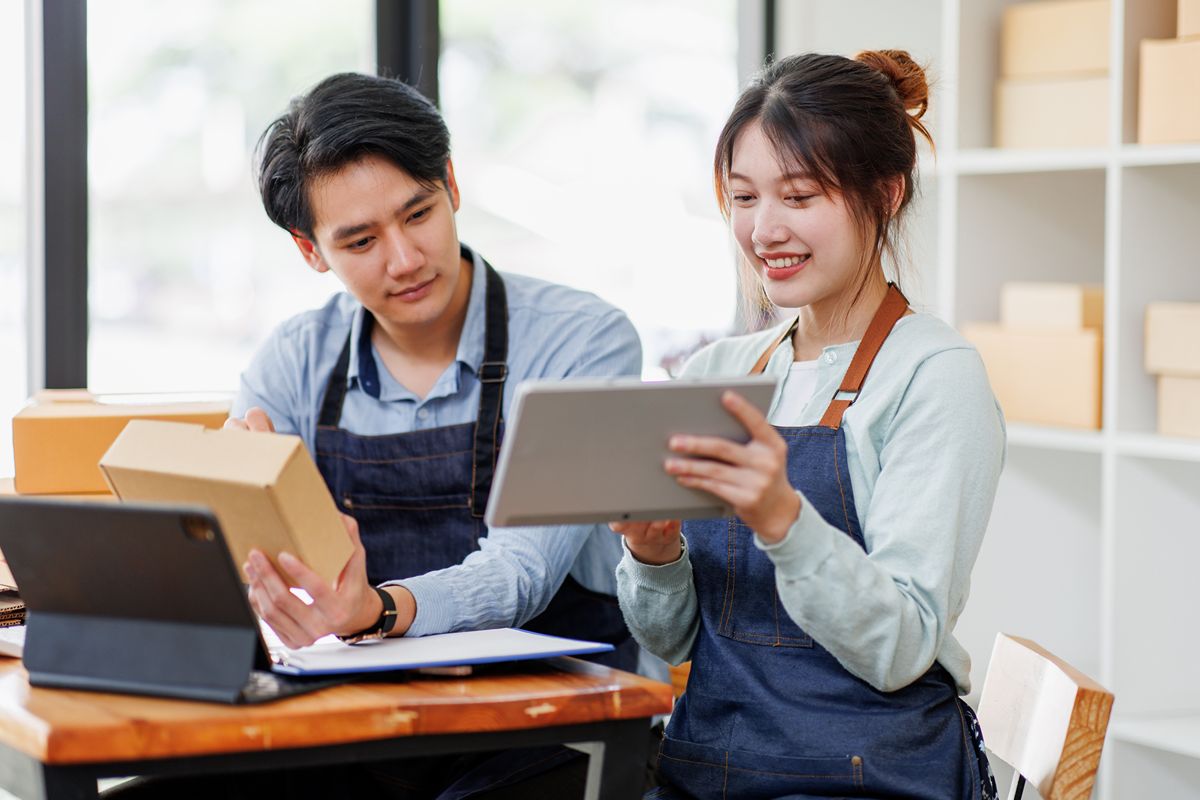 Two warehouse employees reviewing inventory information on a tablet while managing packaged goods